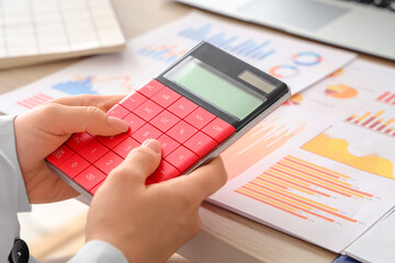 Female accountant with calculator and financial graphics at table in office