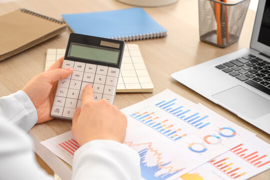 Female accountant with calculator, notebooks, laptop and financial graphics at table in office