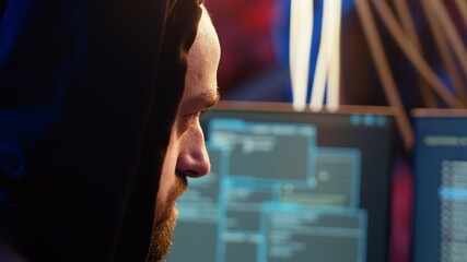 Malicious man hacking, stealing credit card numbers and manipulating banking systems for his own personal gain. Extreme close up of rogue programmer running code in graffiti painted basement, camera B