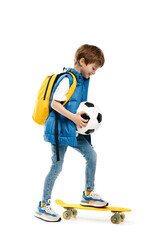Bright little boy with skateboard and backpack holding soccer ball on white background. Back to School.