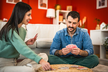 Cheerful boyfriend and girlfriend sit on floor and play cards home
