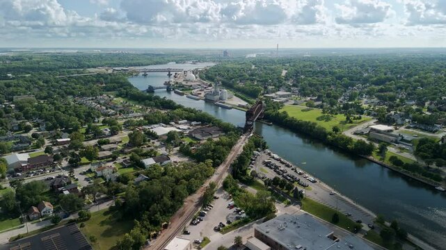 The aerial view of a town divided by a Des Plaines river, with a bridge. The town with lush greenery, a mix of residential, commercial, and industrial buildings. Joliet, Il