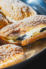Close up view of home-baked eclairs dusted with powdered sugar, filled with cream and blackberries