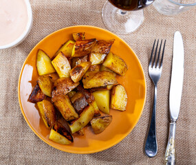 There is portion of sweet potatoes on plate, complemented by bowl with white hot sauce. Traditional Spanish snack