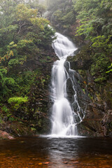 Majestic Waterfall Cascading Down Rocky Cliffs at Glencorse Burn, Pentland Hills Regional Park, Scotland, Surrounded by Lush Greenery and Misty Woodland in a Serene Natural Landscape