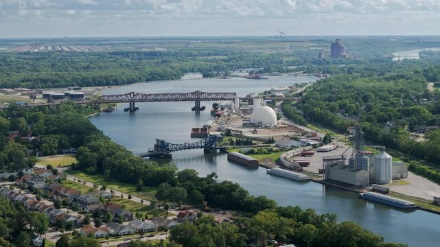 Aerial view of a town divided by a Des Plaines river, with a bridge. The town with lush greenery, a mix of residential, commercial, and industrial buildings. Joliet, Il