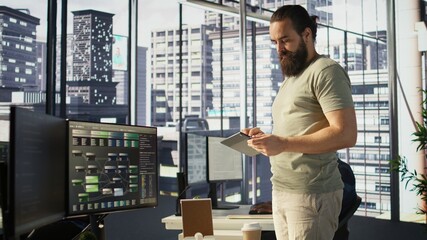 System administrator checking results on tablet after creating complex machine learning models that can process and analyze vast amounts of data. Admin standing in office, looking at device, camera B