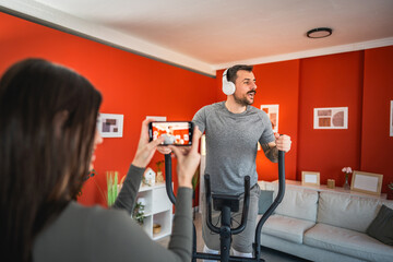 Fototapeta premium woman filming man with mobile phone while he exercise at home