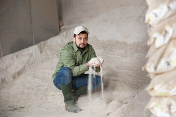 Interested young man livestock breeder checking quality of maize meal in farm storage. Concept of organic supplement in production of compound feed for animals