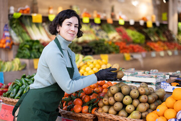 Woman shop assistant puts ripe pear fruits in box on display case, arranges assortment in vegetable shop. Worker puts fruits in pile, in pyramid. Employee makes attractive display case