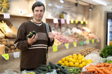 Adult man buyer choosing fresh cucumbers in vegetable shop