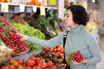 Woman chooses fresh radishes near a vegetable counter in a supermarket. European woman buys...
