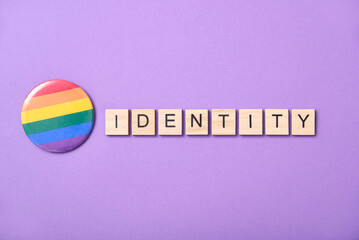 Wooden word Identity beside a rainbow flag button, symbol of LGBT community.