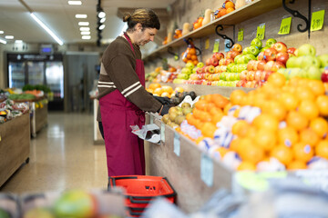 Man shop assistant puts ripe pear fruits in box on display case, arranges assortment in vegetable shop. Worker puts fruits in pile, in pyramid. Employee makes attractive display case