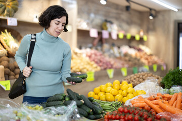 Adult woman buyer choosing fresh cucumbers in vegetable shop
