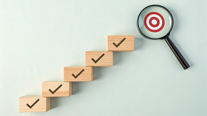 Goal Achievement Steps and Target Concept. Wooden blocks with checkmarks forming a staircase toward a magnifying glass highlighting a target, representing goal achievement and focus. business growth