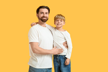 Smiling dad and his little son hugging on yellow background. Father's day