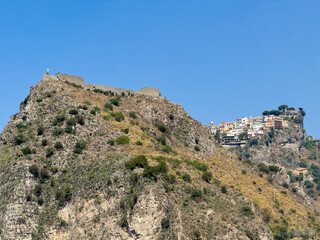 Taormina, Sicily, Italy - July 5, 2024: The Castello on its mountain seen from Ancient Greek theatre or Teatro antico. Cityscape of farther away neighborhood