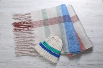 Soft scarf and knitted hat on wooden table, top view