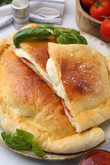 Pieces of delicious calzone pizza with mozzarella, tomatoes and basil on white table, closeup