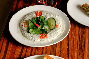 Turkish Haydari on a white plate: creamy yogurt dip with herbs, cucumber, and chili, on a wooden table.