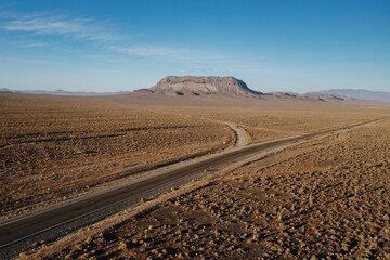 Aerial view of a road cutting through the arid landscape of Nevada, USA, leading towards a mesa. The image captures the vastness and isolation of the desert. Goldfield, Nevada, USA