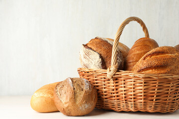 Different freshly baked bread loafs and wicker basket on white wooden table, closeup. Space for text