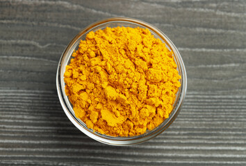 Turmeric powder in glass bowl on grey wooden table, top view
