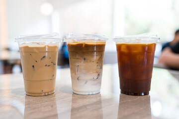 Three plastic cup of iced black coffee, iced cappuccino and iced coffee latte at coffee shop.