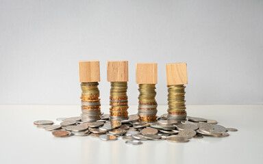 Four blank square wooden blocks in a row on top of stacked coins.