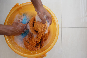 Hands washing cloth in orange tub filled with soap and water