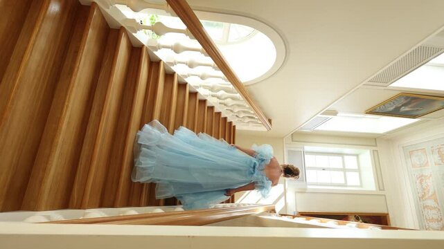 Young beautiful girl in blue dress of Regency era climbs wooden staircase. Classic artistic image of Russian literature of XIX century, outdated.