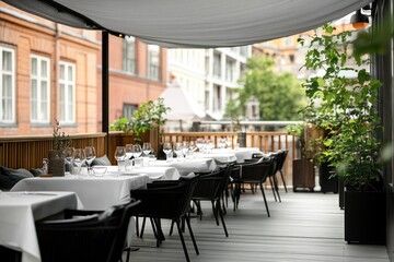 Fototapeta premium Outdoor restaurant patio with white tables, black chairs, and grey awning. City views visible through the canopy.