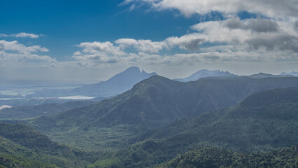 Beautiful panoramic mountain landscape. There is a lush green vegetation, a tropical forest on the slopes and in the valley. Lakes, the ocean are visible in the distance. Blue sky, clouds. Mauritius