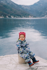Little smiling girl sitting on a bollard on the pier