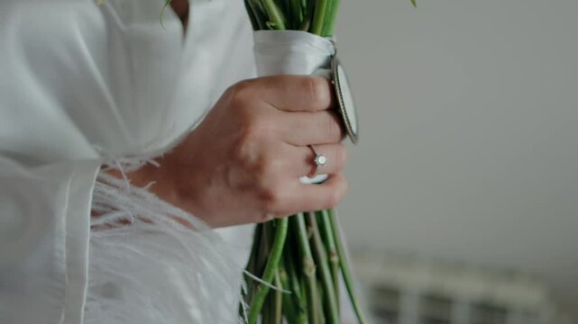 Bride&rsquo;s hand holding bouquet wrapped in white ribbon with sentimental locket