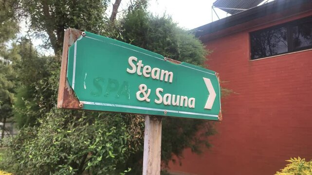 Steam spa and sauna sign low angle with rusty corner on green plastic right arrow