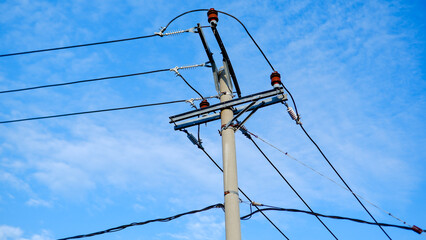 Photo of a concrete electric pole with wires stretching across a bright blue sky. The sturdy pole,...