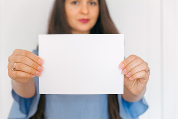 Naklejka premium A young, attractive girl holding mockup with empty paper. A sign, an empty space for advertising, inscription, design. White background.
