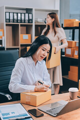 Asian SME business women use laptop computer checking customer order online shipping boxes at home....