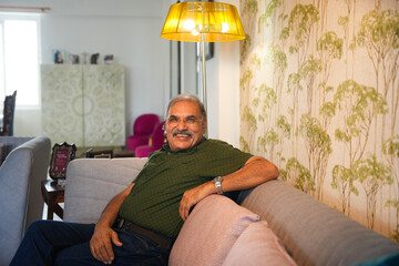 Relaxing retired senior indian man sitting on sofa at home, Happy Elderly male in 60s looking at...