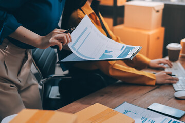 Asian SME business women use laptop computer checking customer order online shipping boxes at home....