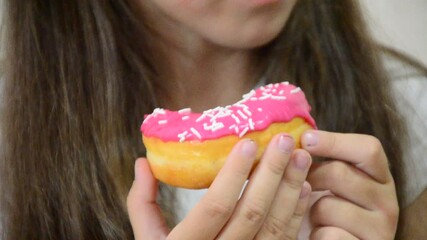 Cute little girl eating pink donut. Girl loves sweets. Funny baby girl eating tasty donut posing. Childhood, fashion. Close-up.
