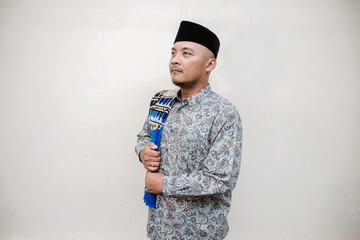 Muslim themed isolated concept photo of a tanned Asian man wearing a paisley or batik patterned...