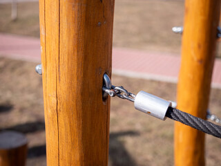 Close-up of a wooden playground post with a black rope securely attached using a metal clamp and eyebolt. 