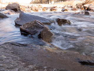 Close-up of a fast-flowing river rushing over dark, textured rocks. The water creates small waves...