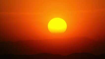 A stunning sunset with a vibrant orange color, featuring the sun setting behind distant mountains.