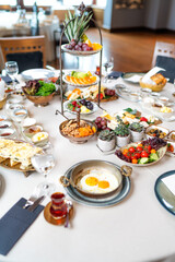 Classic Turkish breakfast in luxury restaurant. Delicious Turkish breakfast served on a round table with fried eggs, fruits, vegetables and drinks. Wide angle photo.Turkey.