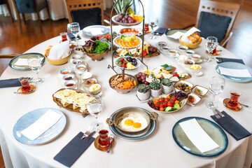 Classic Turkish breakfast in luxury restaurant. Delicious Turkish breakfast served on a round table with fried eggs, fruits, vegetables and drinks. Wide angle photo.Turkey.