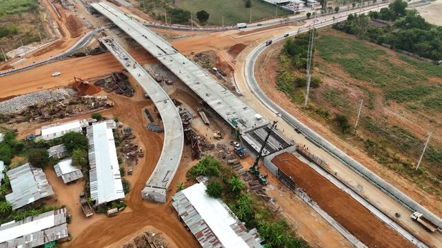 Drone footage of the scenic landscape of the construction site in Thailand. The concrete bridge building over the intersection by crane workers, tractors, and backhoes